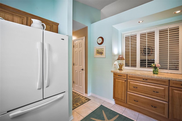 kitchen with light tile patterned floors, a towering ceiling, light stone countertops, and white fridge