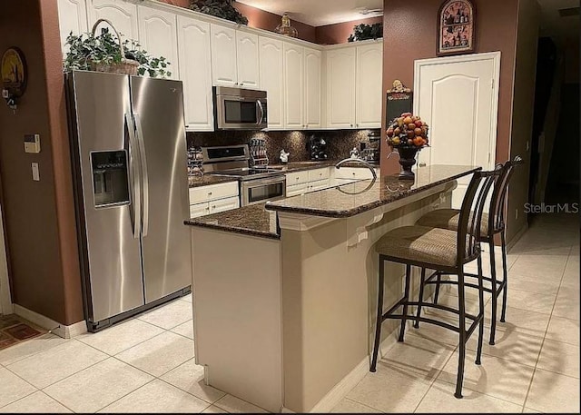 kitchen with dark stone counters, stainless steel appliances, a center island, decorative backsplash, and white cabinets