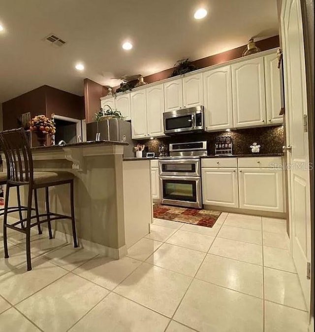 kitchen featuring white cabinetry, a kitchen bar, stainless steel appliances, and light tile patterned flooring