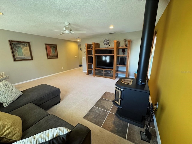 living room featuring baseboards, dark colored carpet, a wood stove, and a ceiling fan