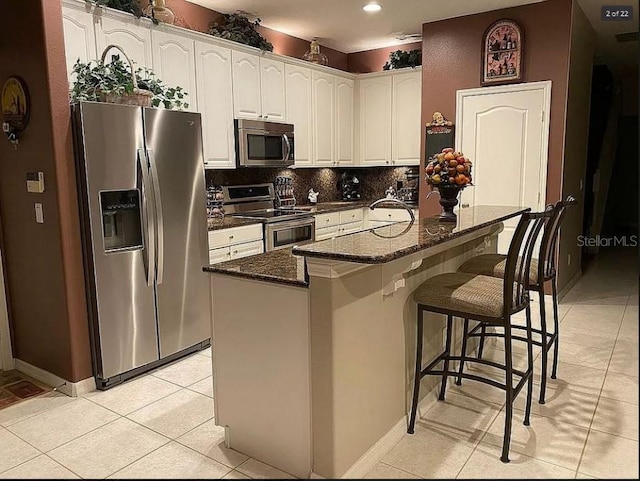 kitchen with light tile patterned floors, tasteful backsplash, a kitchen breakfast bar, stainless steel appliances, and white cabinetry