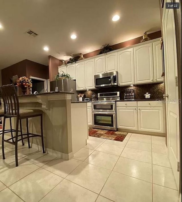 kitchen featuring a breakfast bar, light tile patterned floors, stainless steel appliances, dark countertops, and visible vents