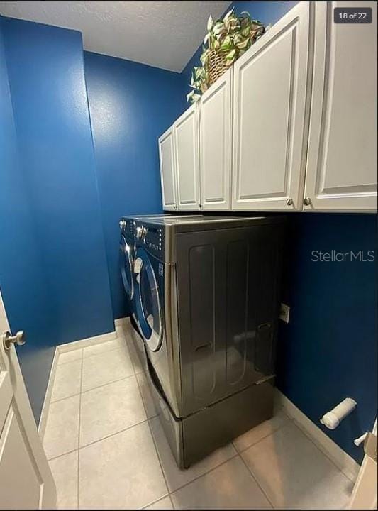 washroom featuring a textured ceiling, baseboards, independent washer and dryer, cabinet space, and tile patterned floors