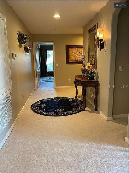 hallway with light carpet, visible vents, and baseboards