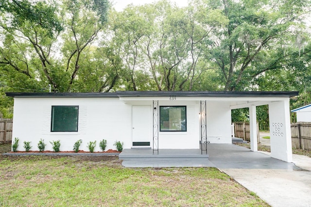 view of front of property with concrete driveway, fence, an attached carport, and a front yard