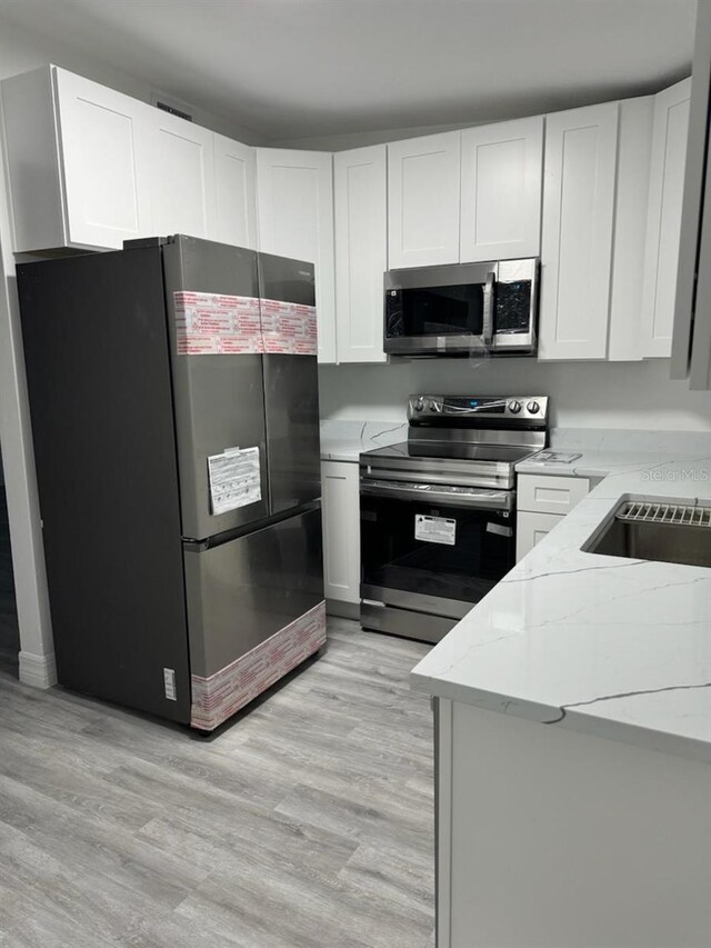 kitchen featuring white cabinets, light stone counters, stainless steel appliances, light hardwood / wood-style floors, and sink