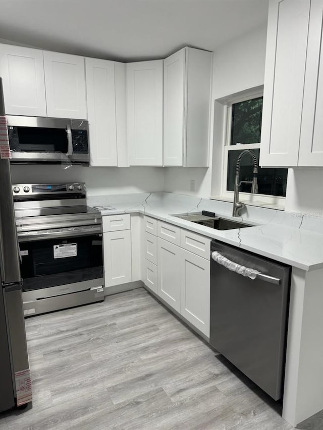 kitchen with light wood-style floors, white cabinets, appliances with stainless steel finishes, light stone counters, and a sink