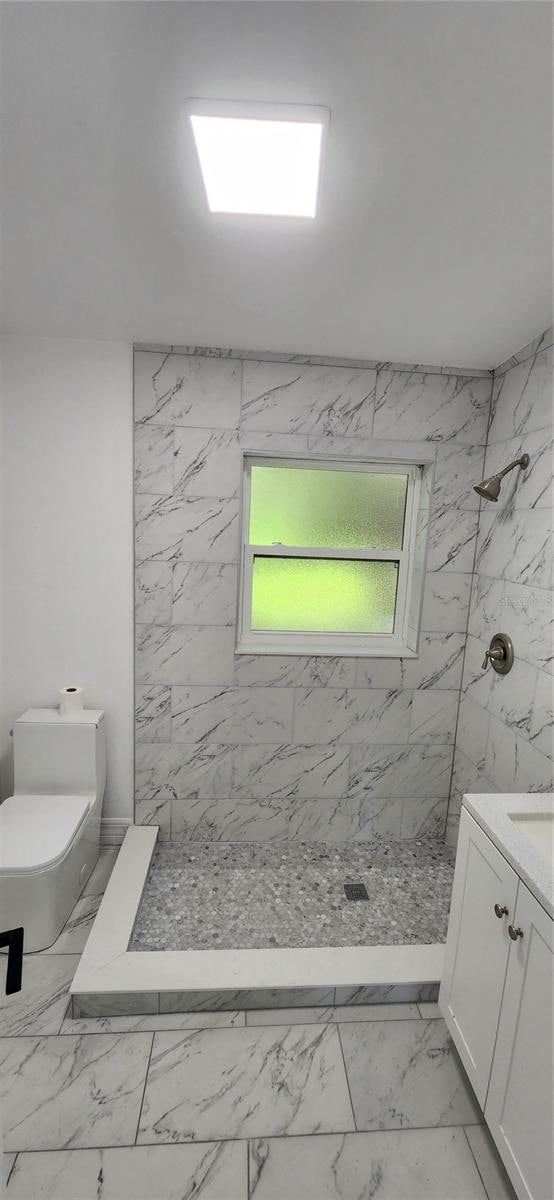 bathroom featuring vanity, a tile shower, toilet, and tile patterned floors