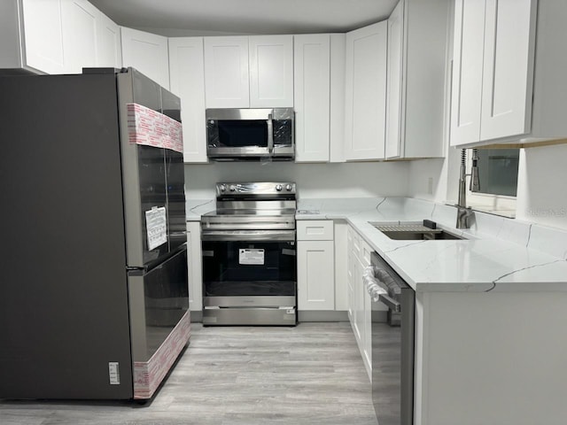 kitchen with light hardwood / wood-style flooring, white cabinetry, light stone countertops, and stainless steel appliances