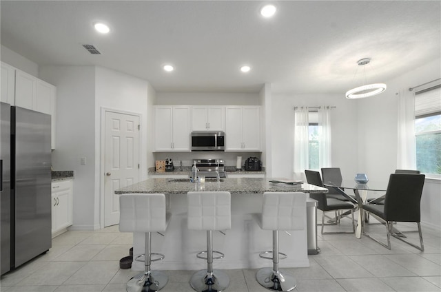 kitchen featuring a wealth of natural light, dark stone countertops, white cabinets, stainless steel appliances, and a center island with sink