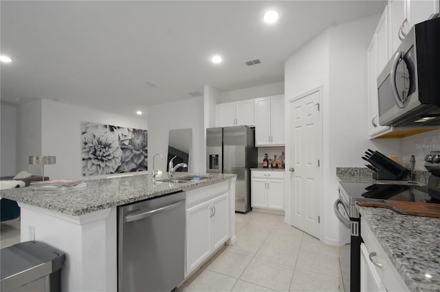 kitchen with appliances with stainless steel finishes, white cabinetry, an island with sink, sink, and light stone countertops