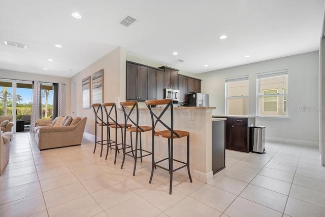 kitchen featuring a breakfast bar, dark brown cabinetry, appliances with stainless steel finishes, and light tile patterned floors