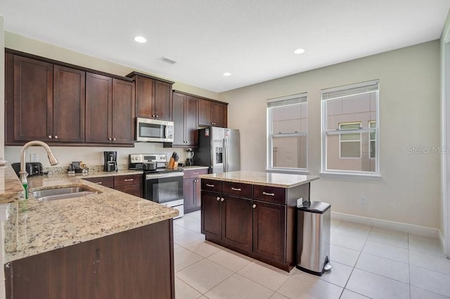 kitchen with appliances with stainless steel finishes, sink, dark brown cabinetry, light tile patterned flooring, and a center island