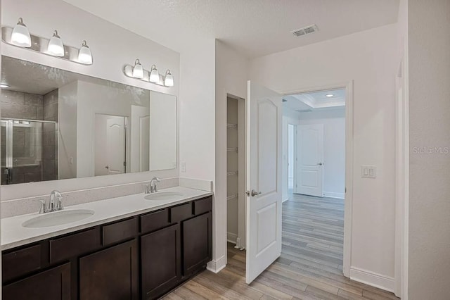 bathroom featuring a shower with shower door, hardwood / wood-style flooring, vanity, a raised ceiling, and a textured ceiling