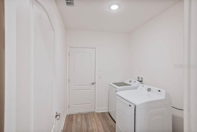 clothes washing area featuring washing machine and clothes dryer and light wood-type flooring