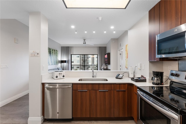 kitchen with ceiling fan, sink, stainless steel appliances, kitchen peninsula, and light hardwood / wood-style floors