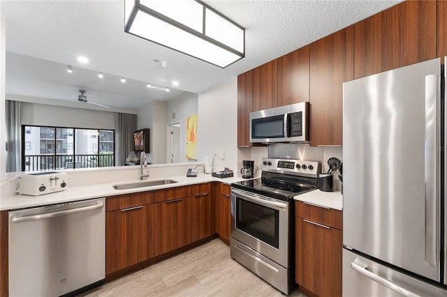 kitchen with appliances with stainless steel finishes, light wood-type flooring, a textured ceiling, ceiling fan, and sink