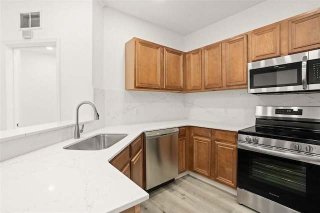 kitchen featuring light wood-type flooring, tasteful backsplash, light stone counters, stainless steel appliances, and sink