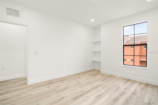 spare room featuring built in shelves and light hardwood / wood-style flooring