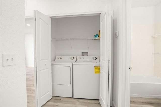 clothes washing area with washer and clothes dryer and light hardwood / wood-style flooring