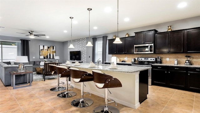 kitchen featuring ceiling fan, hanging light fixtures, stainless steel appliances, an island with sink, and a breakfast bar area