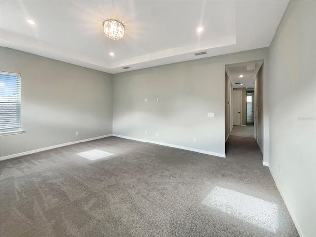 spare room featuring dark carpet, a raised ceiling, and a notable chandelier