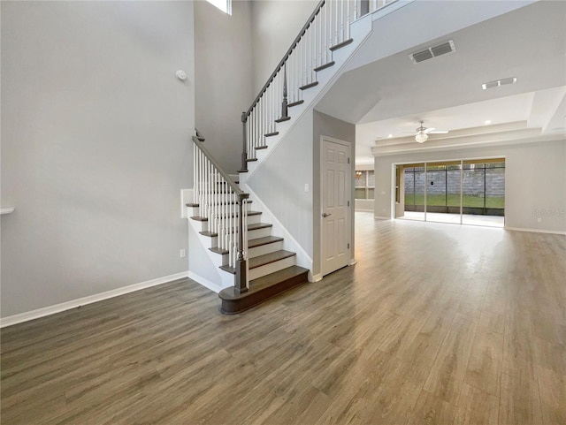 unfurnished living room with a raised ceiling, ceiling fan, hardwood / wood-style floors, and a high ceiling