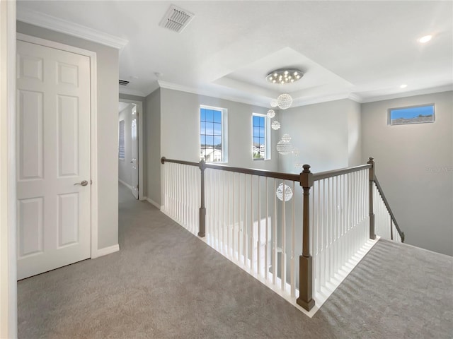 corridor with a tray ceiling, crown molding, carpet, and a notable chandelier