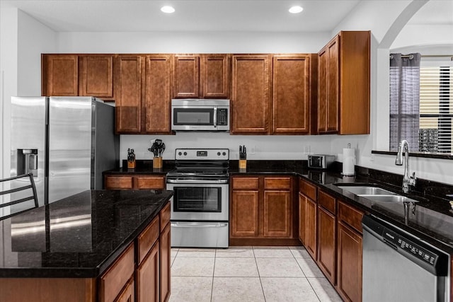 kitchen with dark stone counters, stainless steel appliances, light tile floors, and sink