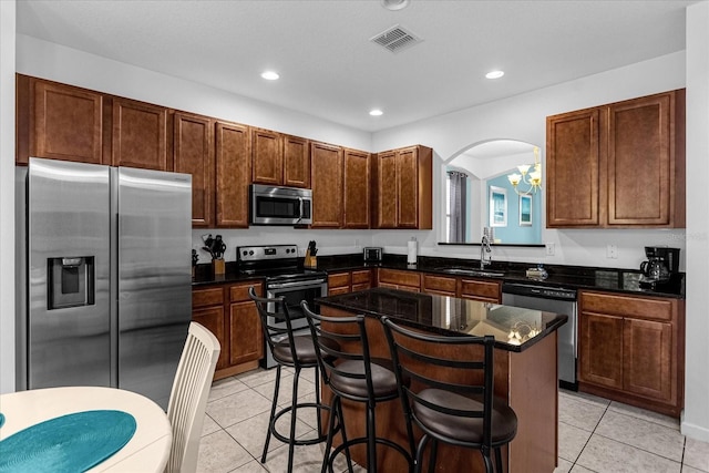 kitchen with sink, appliances with stainless steel finishes, light tile flooring, a notable chandelier, and a center island