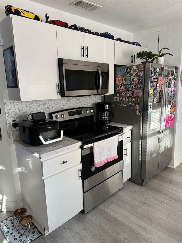 kitchen with tasteful backsplash, white cabinets, light hardwood / wood-style floors, appliances with stainless steel finishes, and a textured ceiling