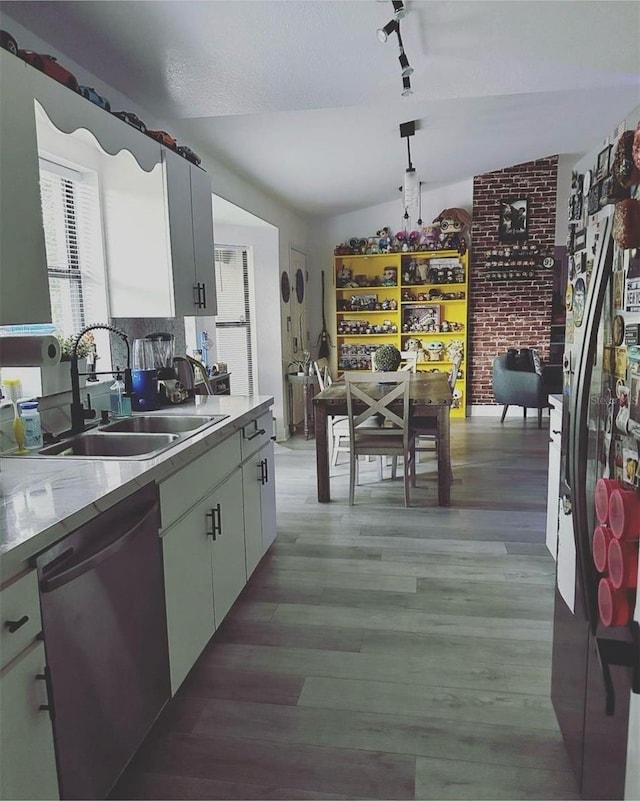 kitchen featuring stainless steel dishwasher, light hardwood / wood-style floors, track lighting, vaulted ceiling, and sink