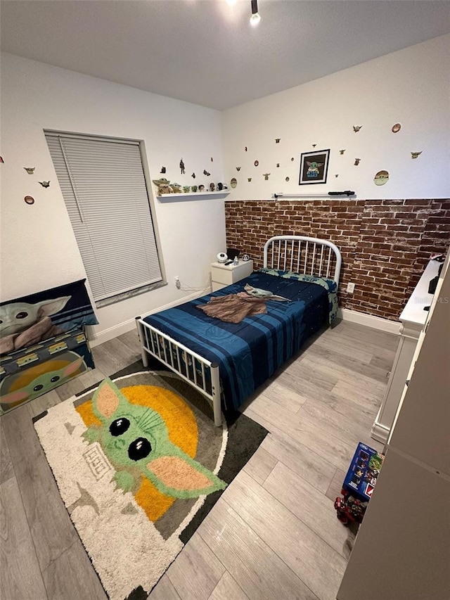 bedroom with wood-type flooring and brick wall