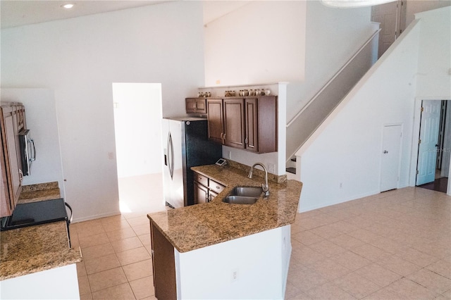 kitchen featuring high vaulted ceiling, stainless steel fridge with ice dispenser, sink, and light stone countertops