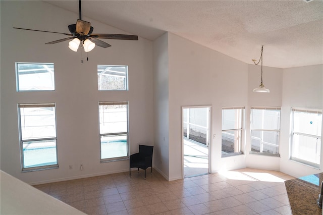 unfurnished living room with ceiling fan, high vaulted ceiling, a textured ceiling, and light tile patterned floors