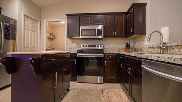 kitchen featuring dark brown cabinetry, stainless steel appliances, a sink, light countertops, and light wood finished floors