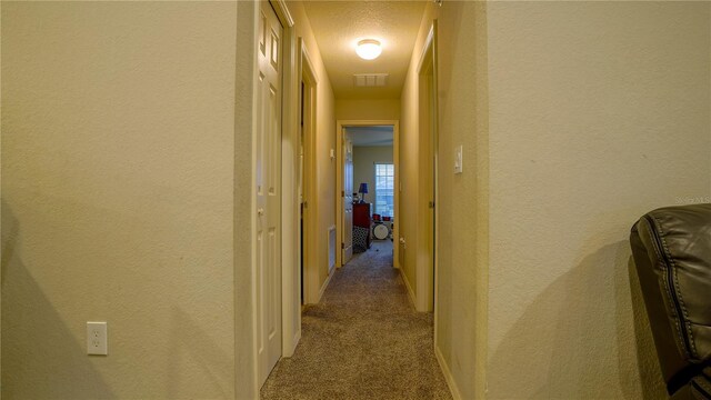 hallway featuring carpet, visible vents, a textured wall, and a textured ceiling