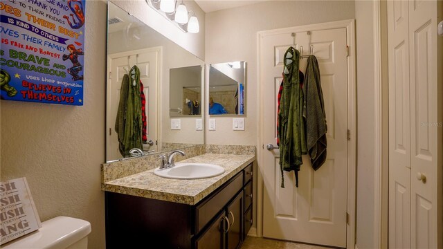 bathroom with toilet, a textured wall, visible vents, and vanity