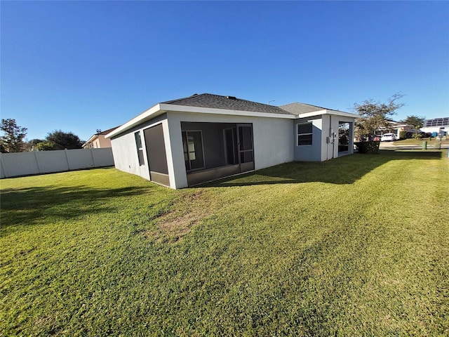 rear view of property featuring a lawn, fence, and stucco siding