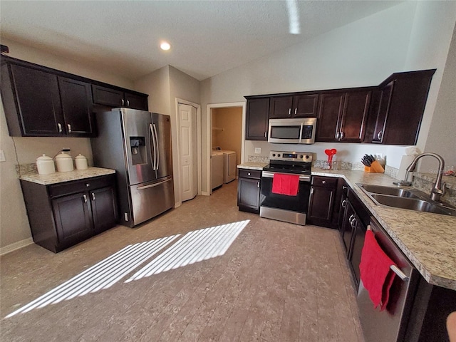 kitchen with a sink, vaulted ceiling, light countertops, appliances with stainless steel finishes, and washing machine and clothes dryer