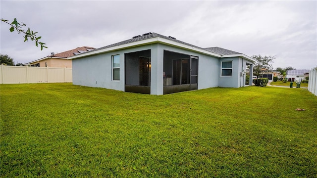 back of property with a sunroom, stucco siding, a lawn, and fence