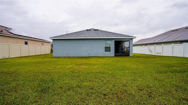 rear view of property featuring a shingled roof, a lawn, a fenced backyard, and stucco siding