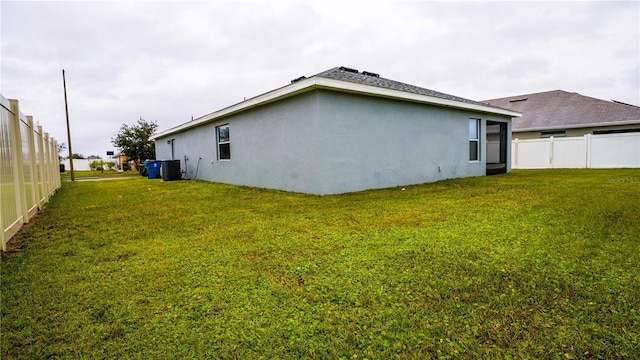 rear view of house with a yard, stucco siding, fence, and central air condition unit