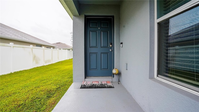 property entrance with a yard, fence, and stucco siding