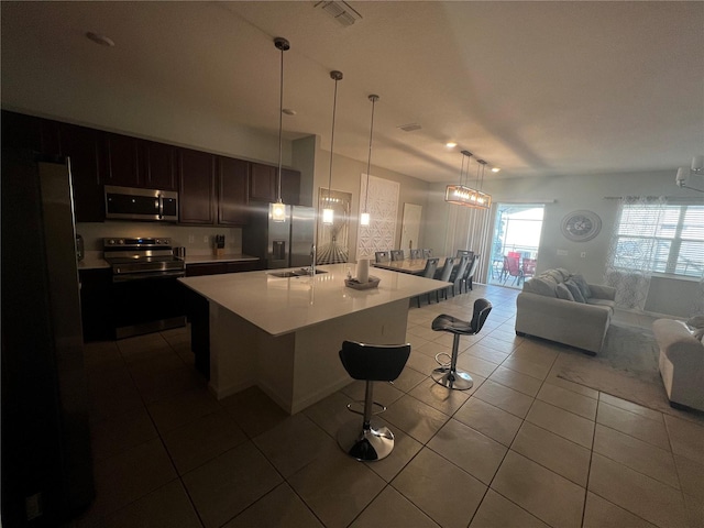 kitchen with dark brown cabinets, a kitchen bar, a center island, stainless steel appliances, and hanging light fixtures