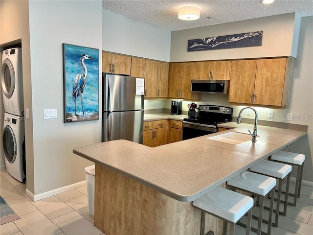 kitchen with appliances with stainless steel finishes, a kitchen breakfast bar, stacked washer and clothes dryer, sink, and kitchen peninsula