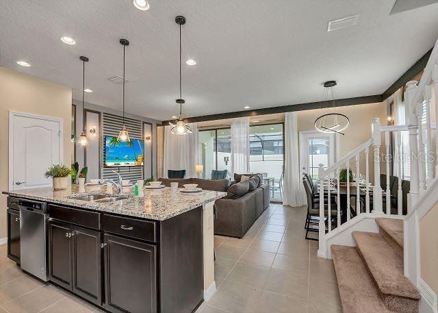 kitchen with sink, decorative light fixtures, light tile patterned floors, stainless steel dishwasher, and a kitchen island with sink