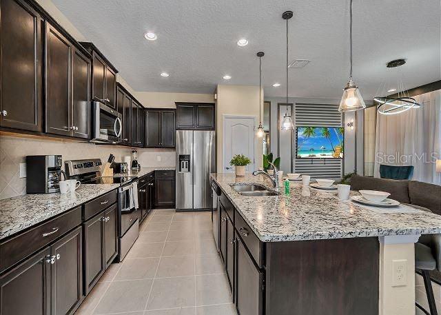 kitchen featuring appliances with stainless steel finishes, decorative light fixtures, sink, a kitchen breakfast bar, and a center island with sink