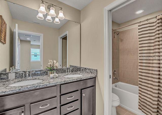 full bathroom featuring shower / tub combo with curtain, tile patterned floors, toilet, a chandelier, and vanity