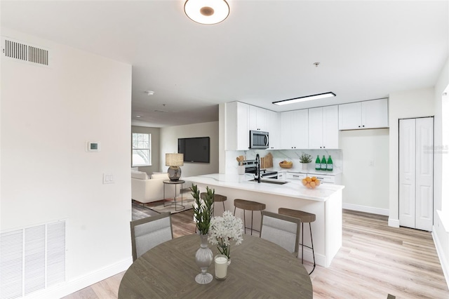 kitchen featuring kitchen peninsula, appliances with stainless steel finishes, light wood-type flooring, a kitchen breakfast bar, and white cabinets